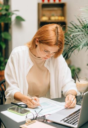 Woman analyzing financial documents using laptop and calculator indoors.